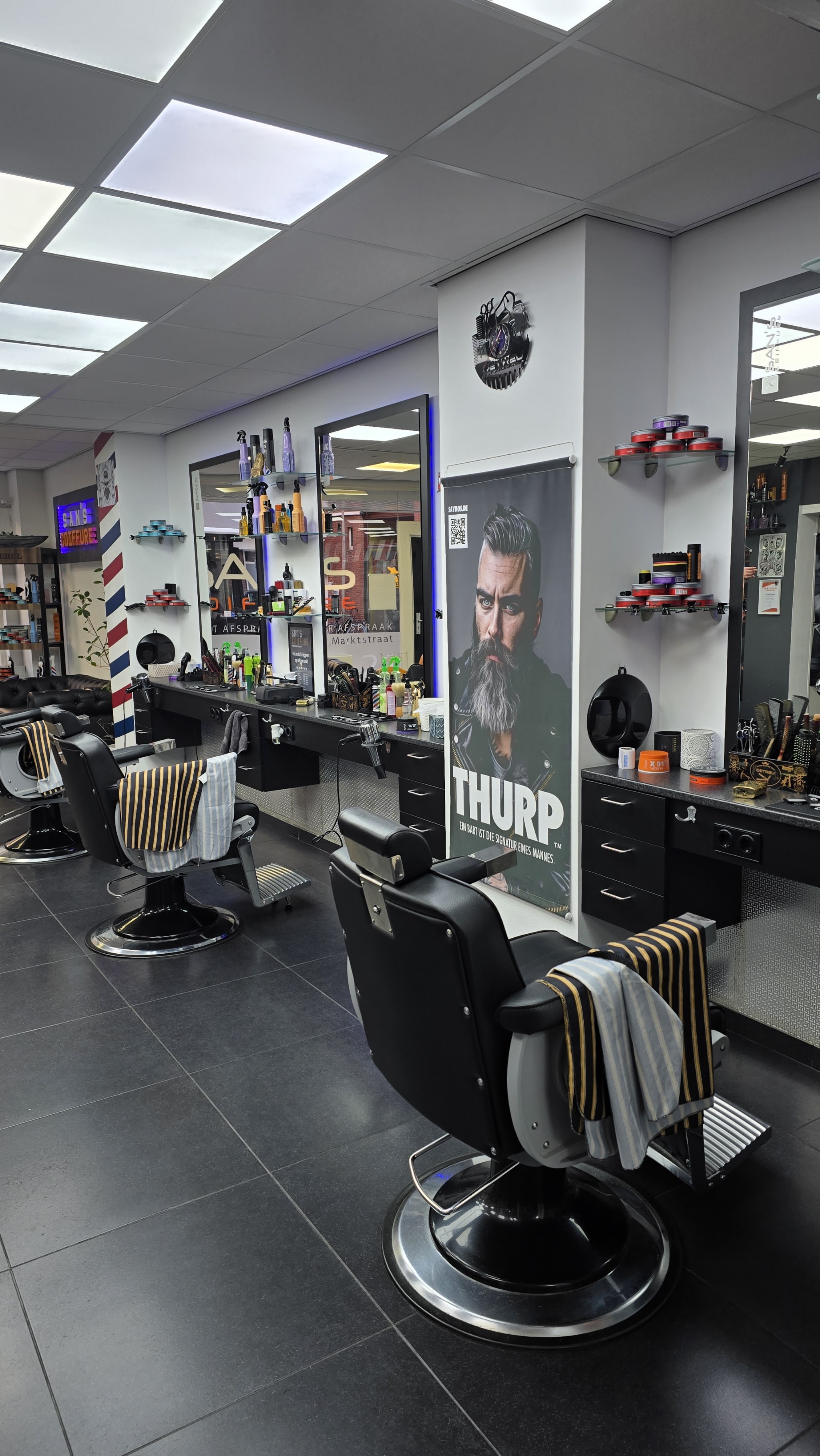 De kapsalon van binnen: zwarte barberstoelen voor de spiegels