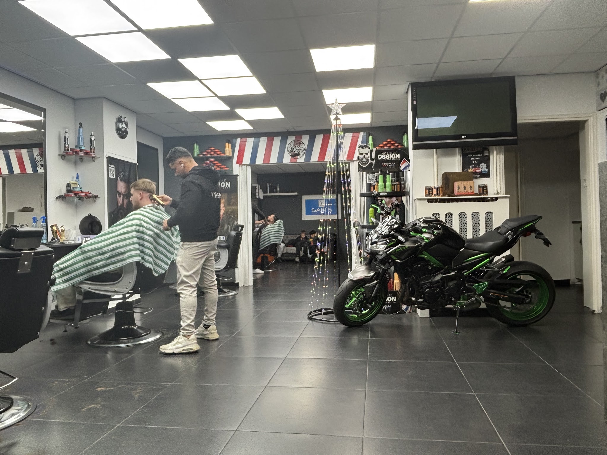 Een barber knipt een klant in een gestreepte kapmantel, met een motor in de zaak